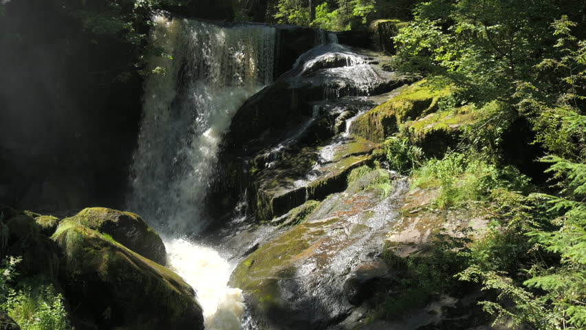 The highest waterfall of the Black Forest in Triberg, Germany. Slow motion of falling clear mountain water in detail. Big rocky stones covered with green moss in a mountain place