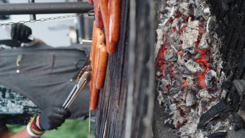 Sausages, street food, grilled on a charcoal grill. Grilled sausages roasting on barbecue grill outdoors. BBQ. Turn sausages over. concept street food for picnic and camping. Vertical video.