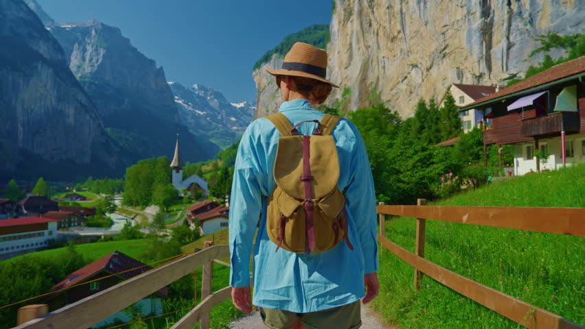 Lauterbrunnen, Switzerland. A young tourist with a backpack walks along the incredible views of a famous Swiss village with a waterfall in the Alpine mountains
