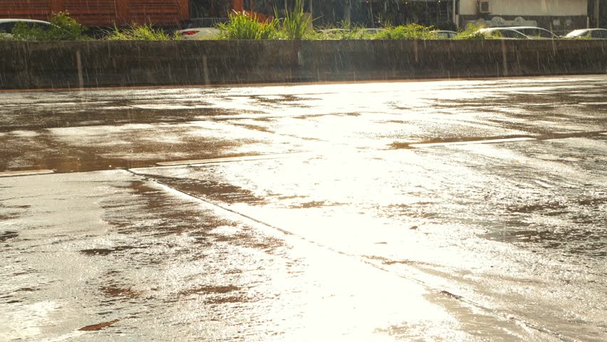 Motorbikes and cars are driving on the wet road after the rain, person is walking. The sun is shining it is raining. Chiang Mai, Thailand