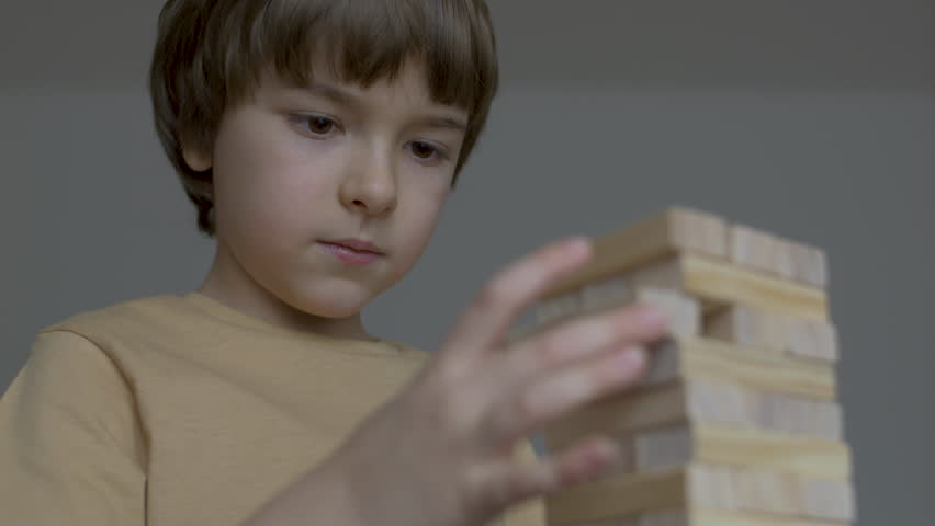 Child Having Fun Building Constructor Tower of Wooden Blocks. Boy Playing Wooden Block Tower Game at Home. Board Creative Game. Child Development Education Leisure. Play With Wooden Building Blocks.