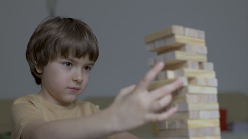 Child Having Fun Building Constructor Tower of Wooden Blocks. Boy Playing Wooden Block Tower Game at Home. Board Creative Game. Child Development Education Leisure. Play With Wooden Building Blocks.