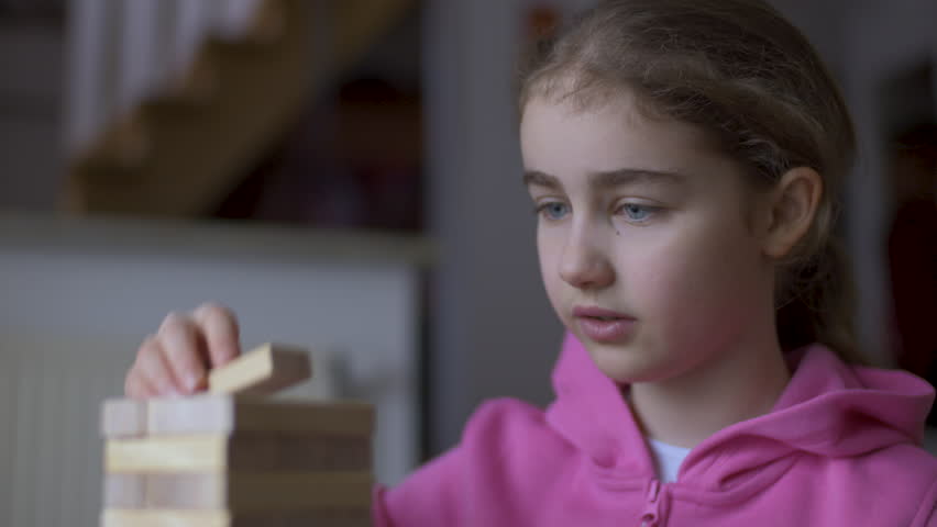Child Having Fun Building Constructor Tower of Wooden Blocks. Girl Playing Wooden Block Tower Game at Home. Board Creative Game. Child Development Education Leisure. Play With Wooden Building Blocks.