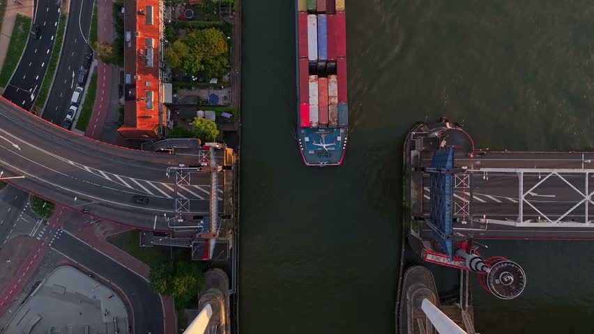 Top down view of a container barge sailing between an open bridge on a sunny evening.