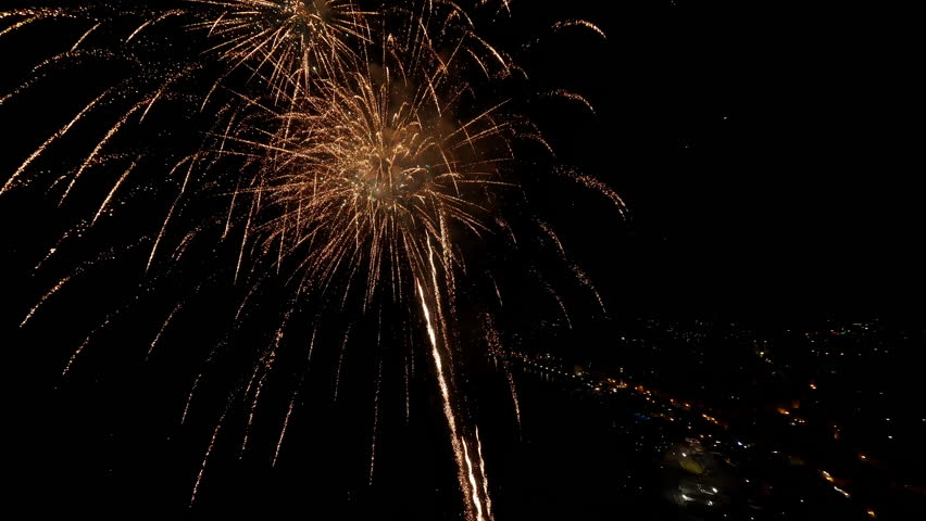 Golden fireworks explode against a night sky over a cityscape, creating a dazzling display