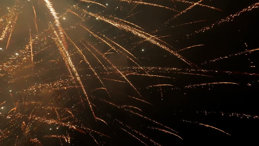 Golden fireworks explode against a night sky over a cityscape, creating a dazzling display