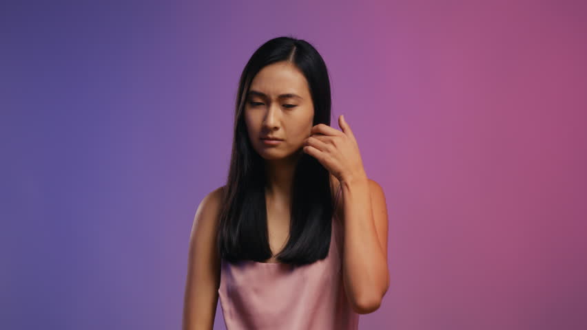 Young Asian woman looking at her long hair, unhappy with her haircare routine