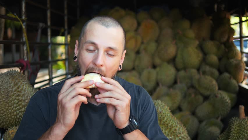 Handsome Man Enjoying Eating Delicious Fresh Durian, Texture of Durian Fruit, Durian Fruits Background. New Experience, Travel, and Boldness Concept