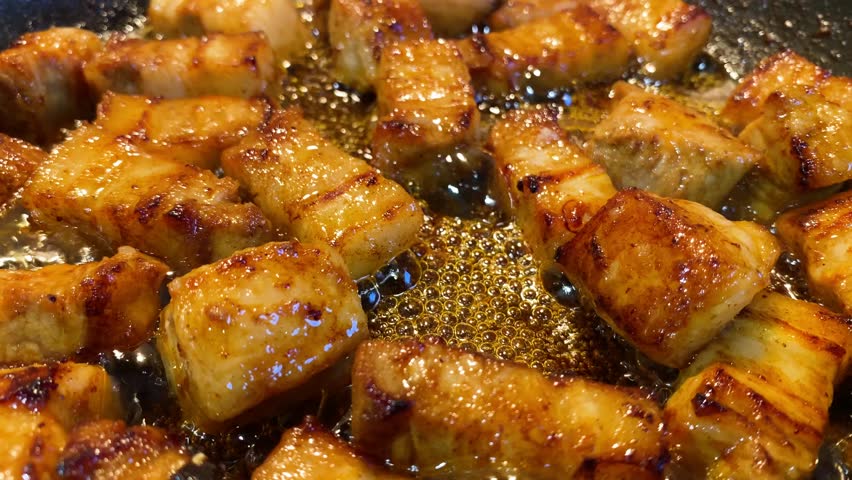 Close up of seasoned Belly Pork sizzling in oil in a frying pan. Static.