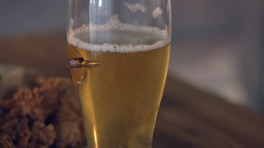 A close-up of an unusual glass of beer with a bullet sticking out of the glass.