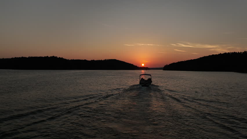 Flyover Of Boat Riding Towards Bright Orange Sunset On Arkansas Lake, Aerial View