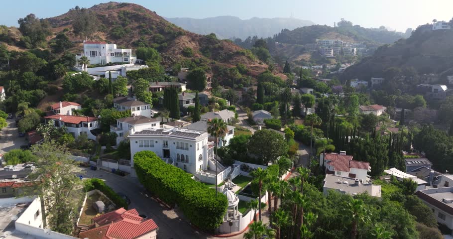 Aerial dolly above large mansion homes up winding road on hillside of Los Angeles California