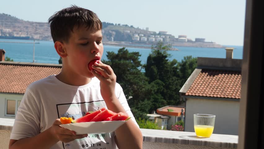 boy eats fresh fruits and vegetables on the balcony overlooking the sea. A beautiful, healthy, low-calorie breakfast or snack on vacation.  low calories delicious desserts. Summer fresh fruit.