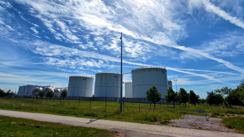 Large industrial storage tanks with a blue sky and contrails in the background