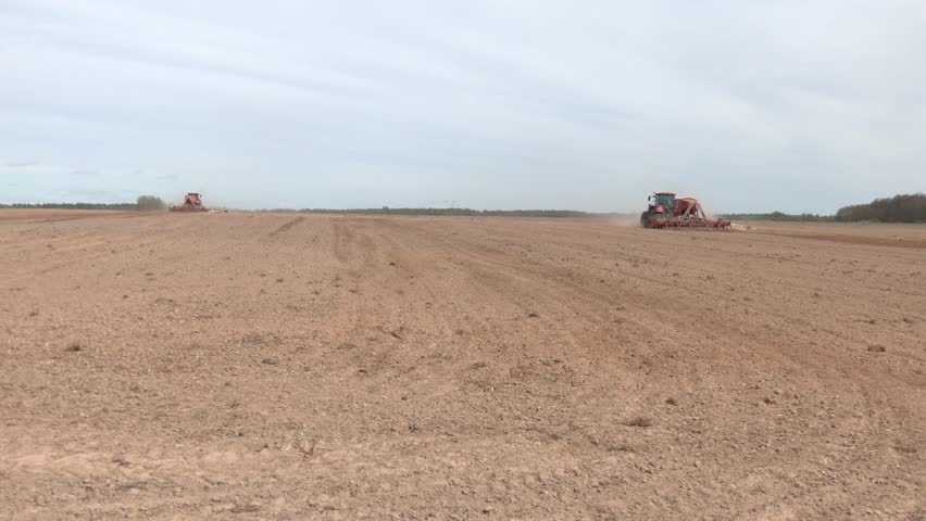 Two tractors on the field in a sunny day. Preparing land for sowing. Agricultural works at farmlands. Tractor ploughing a field with a dust behind it. Agriculture industry
