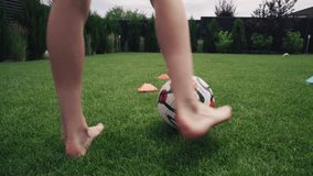 Young soccer player dribbles football ball through orange disc cones. Athletic teen boy trains outside in house courtyard on grass lawn, prepares for championship. Hobby and sports. Knee level shot. - Powered by Shutterstock - Get 15% off with code: PIKWIZARD15