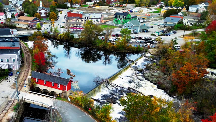 The historic dam and mill straddling the South Berwick, Maine and Somersworth, NH border are framed by vibrant autumn foliage, creating a picturesque fall scene.