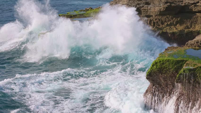 Rotating aerial shot of massive waves crashing against rugged cliffs on Lembongan Island, Bali. Captures the raw power of the ocean and dramatic coastal scenery.