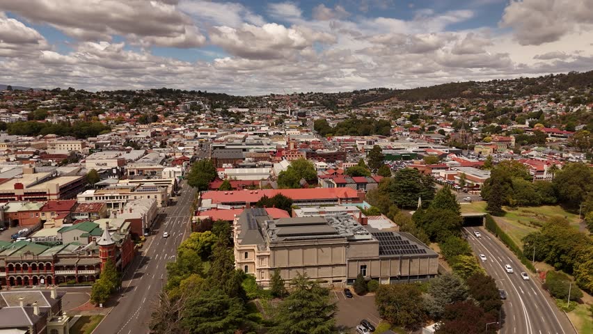 Traffic on intersection in city of Launceston, Tasmania during cloudy day in summer. Roofing flight over downtown with buildings and homes. Aerial wide shot.