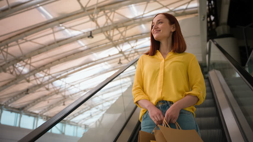 Happy joyful glad Caucasian female woman girl shopper client customer consumer tourist hold many paper bags enjoy shopping after flight riding escalator moving stairs inside shop mall airport terminal