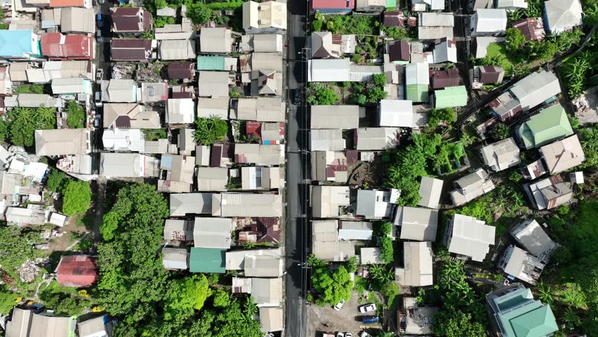 Narrow urban street lined with dense, low-roofed houses in a tightly packed residential neighborhood. Aerial top down shot. Impoverished low-income third-world country.