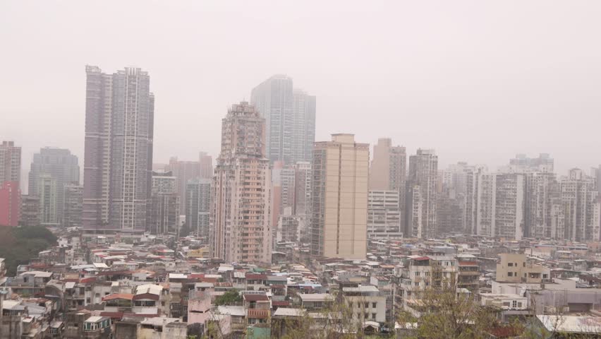 A misty and overcast view of the Macau cityscape in China, featuring numerous skyscrapers and densely packed buildings.