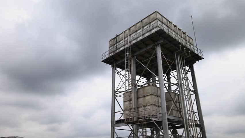 Aerial establishing shot of a large water storage metallic structure with containers at a factory