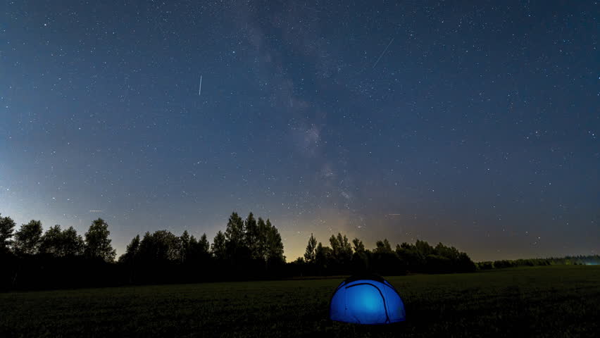 Time Lapse of Milky Way Moving over blue Glowing Tent. Night Starry Sky 