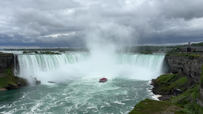A tour boat loaded with tourists in red ponchos cruises towards to mist at the base of the Horseshoe Falls in Niagara Falls Ontario.