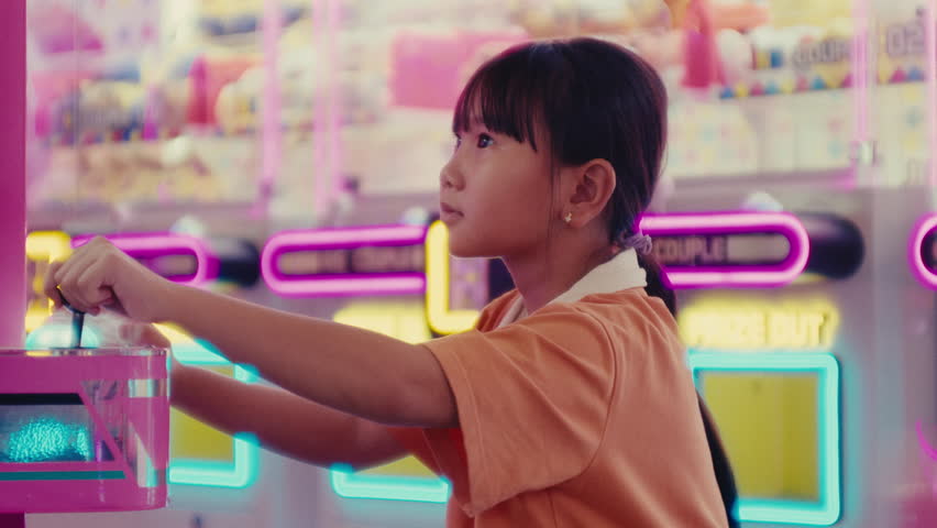 little adorable cute asiatic girl female kid playing video games in game room amusement park having fun during a funny holiday weekend day