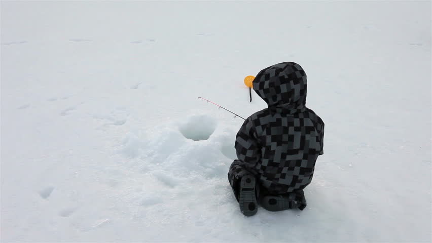 Young boy ice fishing on winter lake.