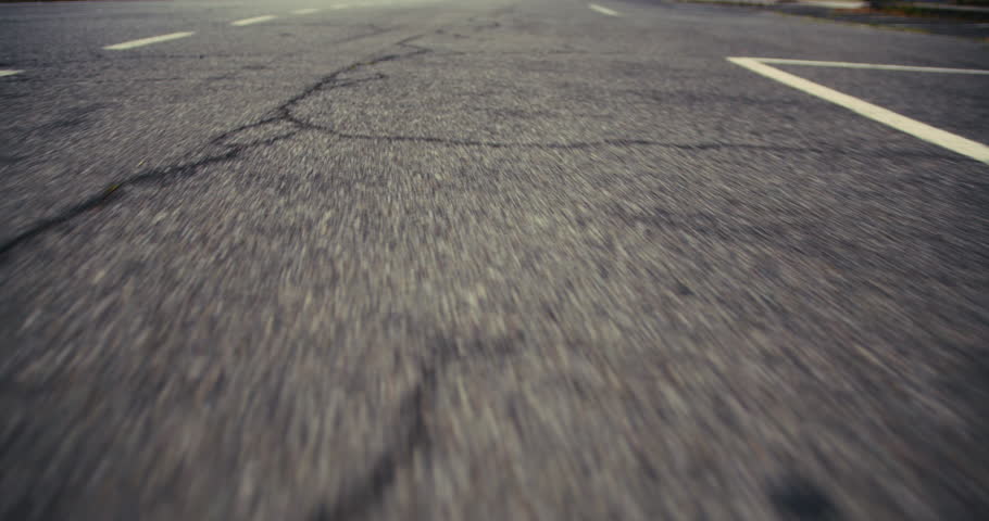 A low-angle, dynamic shot of a rural asphalt road at dusk, capturing the texture of the pavement as the vehicle swiftly moves forward, emphasizing the journey and the solitude of the empty street.