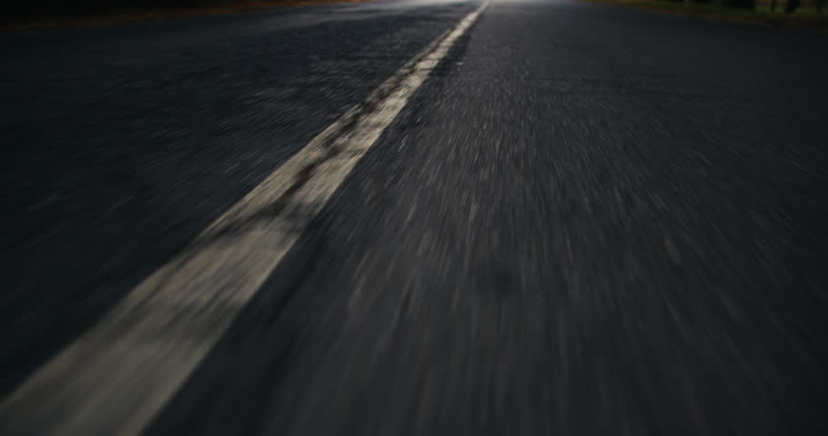 POV shot of a dark, cracked asphalt road at night, capturing the motion and atmosphere of a nighttime drive on a dimly lit, empty street.