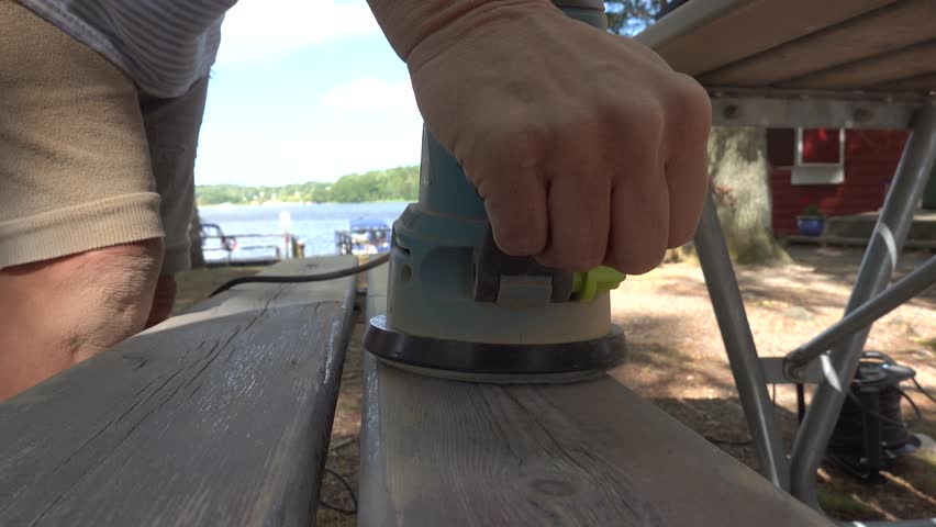 Stockholm, Sweden A man uses an electric sanding machine to refinish a wooden picnic table.