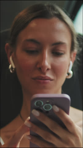 Vertical video, Young brown-haired woman with headphones listens to music, uses mobile phone during train ride