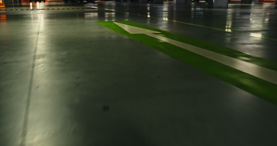 Dynamic, low-angle camera movement captures the reflective floor of an underground parking garage, showcasing traffic signs and directional arrows as the camera glides smoothly along the floor.