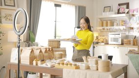 Asian woman bakery shop owner live streaming on smartphone presentation sell homemade food and bakery in the kitchen. Small business e-commerce online catering shop food and drink entrepreneur concept - Powered by Shutterstock - Get 15% off with code: PIKWIZARD15