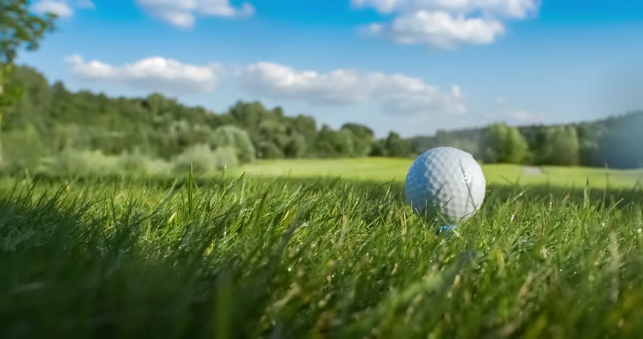 Golf club hits a golf ball in a super slow motion. Drops of morning dew and grass particles rise into the air after the impact.