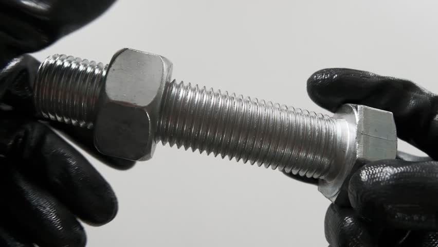 Thread control, a bolt in the hands of black gloves. Checking the quality of the threaded thread with a nut of the appropriate size.