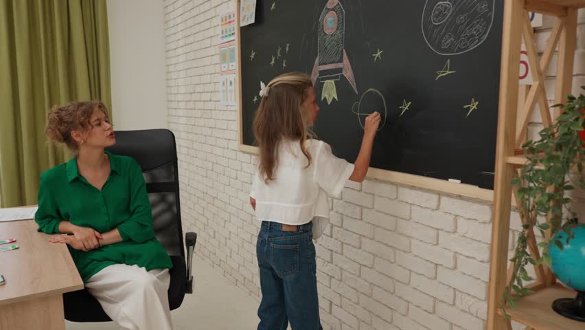 Junior school boys and girls sit in room during astronomy class. Girl comes to board and draws planet on chalkboard. Modern education concept.