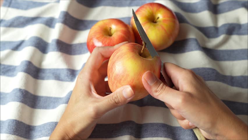 Woman peels an apple with a knife above the old rag