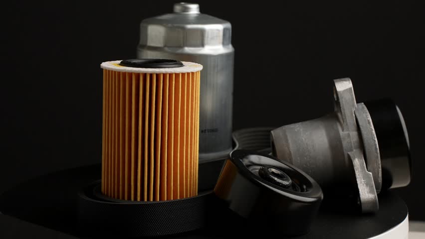 Slowly rotating auto parts on black background. Fuel, oil filters and tension roller with poly V-belt are rotating around. Auto parts replacement concept.