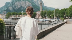 Young brown-haired woman dressed in white shirt, walking along the embankment along the lake, view from behind - Powered by Shutterstock - Get 15% off with code: PIKWIZARD15