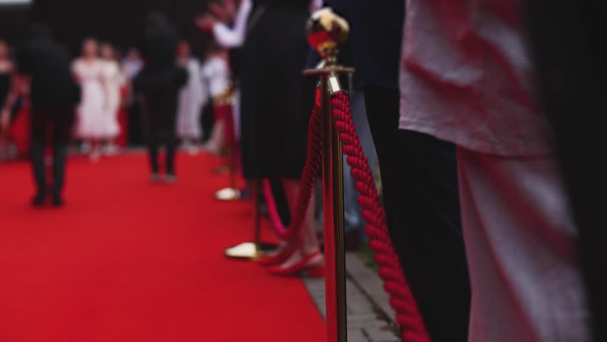 Red carpet with ropes and golden barriers on a luxury party entrance, cinema premiere film festival event award gala ceremony, wealthy rich guests arriving, outdoor decoration elements, summer day