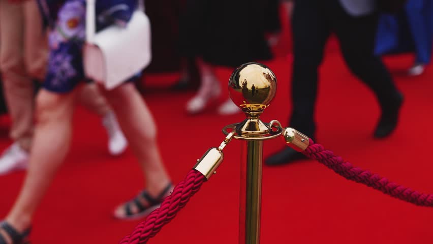 Red carpet with ropes and golden barriers on a luxury party entrance, cinema premiere film festival event award gala ceremony, wealthy rich guests arriving, outdoor decoration elements, summer day