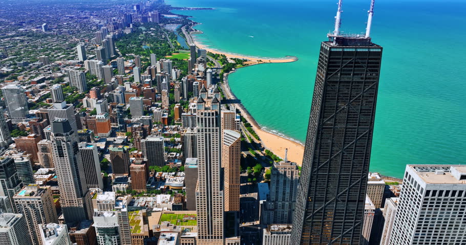 Dark skyscraper of the John Hancock Center towering above the gorgeous cityscape. Drone footage above the Lakeshore Drive approaching waterscape of Lake Michigan on sunny day.