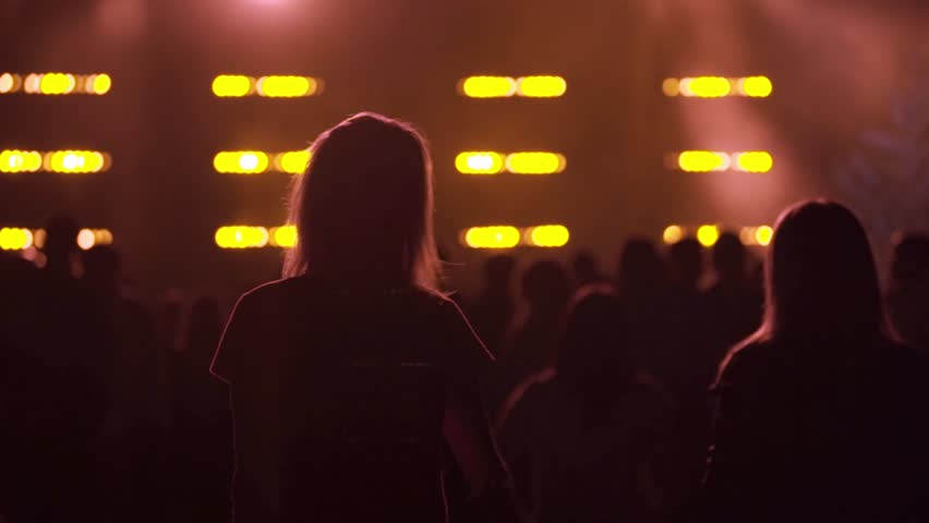 Silhouettes of people dancing and enjoying a night concert with bright lights creating an electrifying atmosphere.