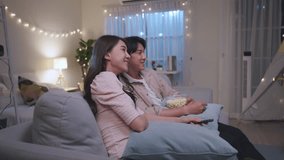 Asian young loving couple watch movie together in living room at home. Attractive new marriage man and woman having fun, sitting on sofa watch comedy video on TV during weekend activity in house. - Powered by Shutterstock - Get 15% off with code: PIKWIZARD15