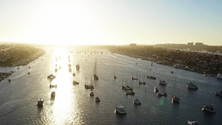 Aerial tracking shot of sailboats glistening at sunset in Newport Bay, Cali