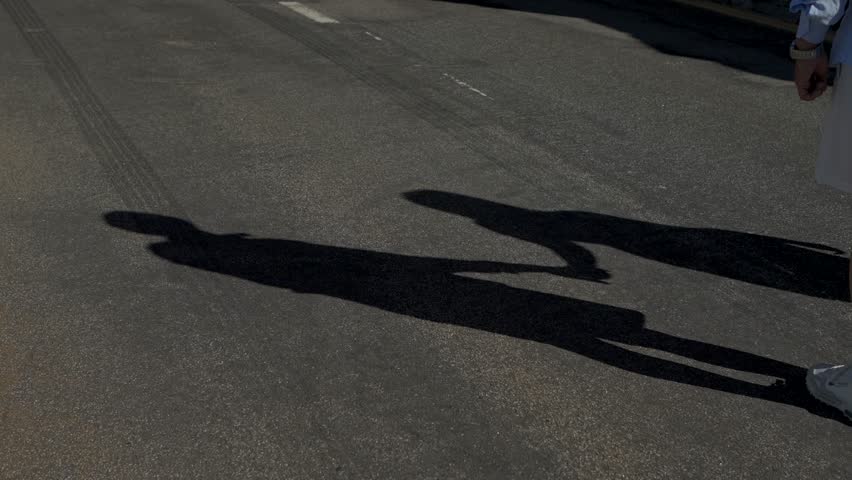 Silhouette of a couple holding hands, casting shadows on the pavement in bright sunlight